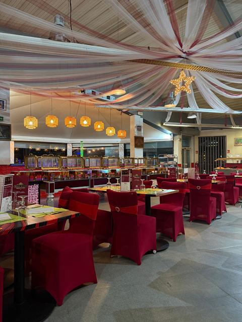 Rangée de lanternes dorées au-dessus du buffet aux chauffe-plats dorés, tables dressées et chaises bordeaux